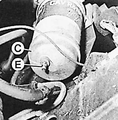 1. Подставить под топливный фильтр емкость, ослабить сливной болт (Е) и болт крепления трубопровода…